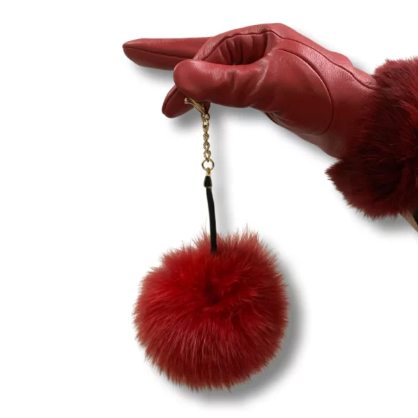 A red leather glove wearing hand holds a red fox pom pom keychain