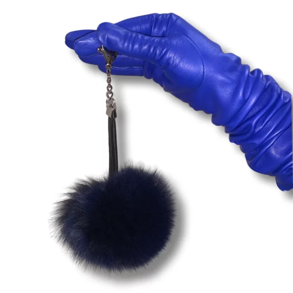Blue leather glove wearing hand holds a dark blue fox pom pom keychain