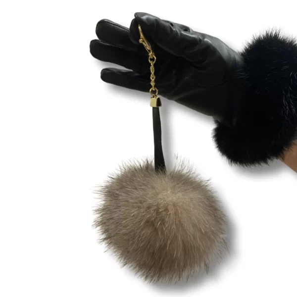 A black leather glove wearing hand holds a fox pom pom keychain