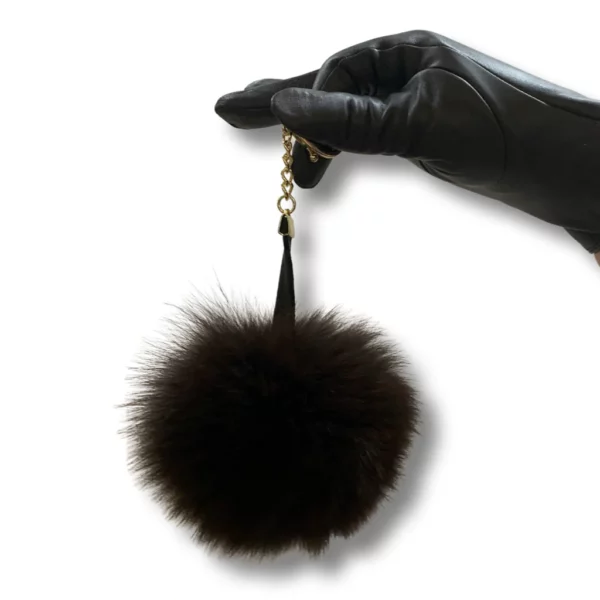 Black leather glove wearing hand holds a black fox pom pom keychain
