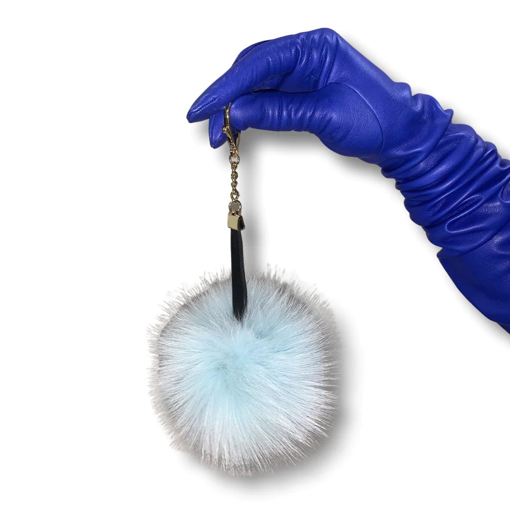 Blue leather glove wearing hand holds a teal fox pom pom keychain