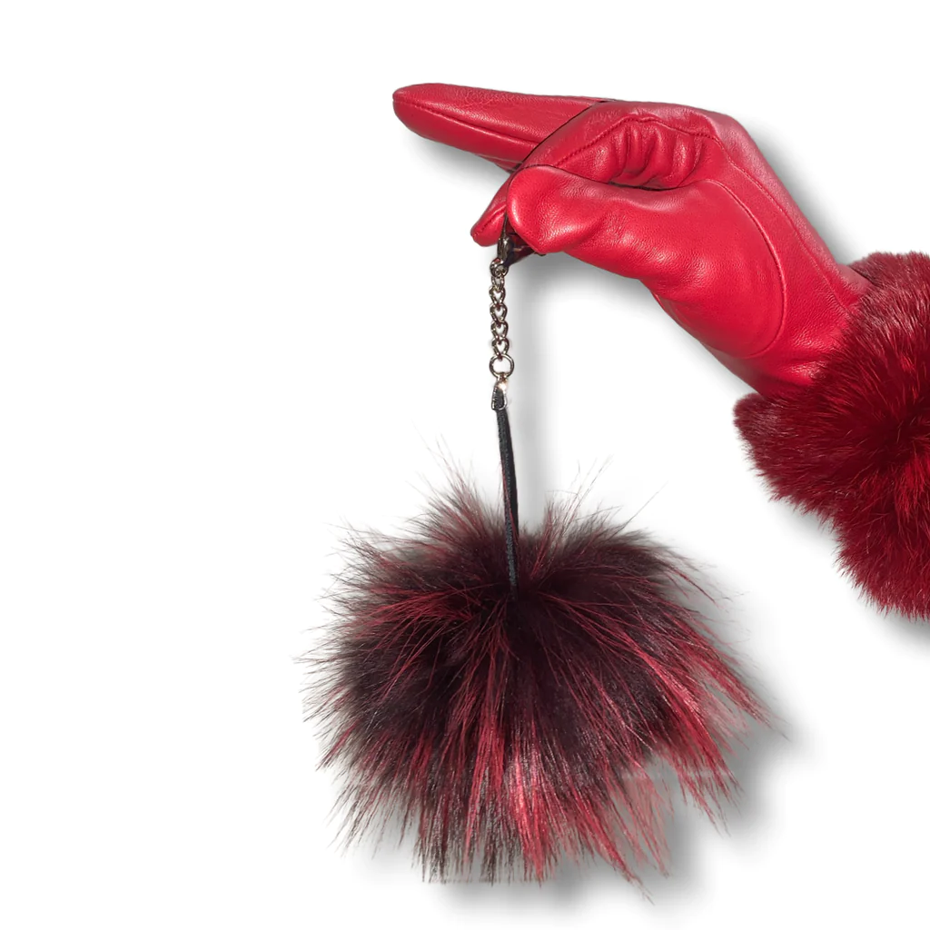 Red leather glove wearing hand holds a red fox pom pom keychain