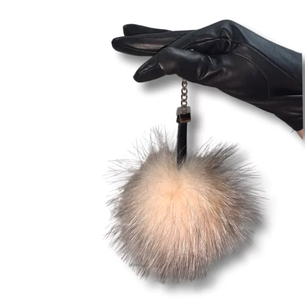 Black leather glove wearing hand holds a pink fox pom pom keychain