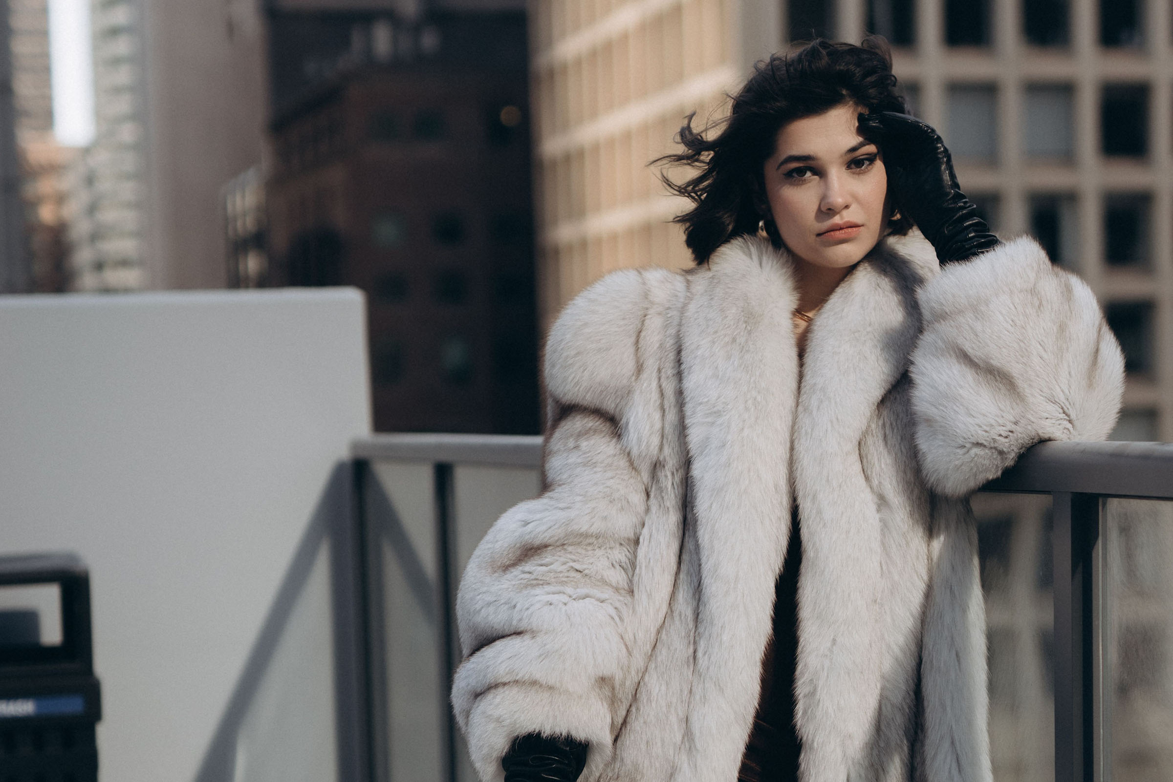 Black-haired woman in a fur coat holds a gloved hand to her face