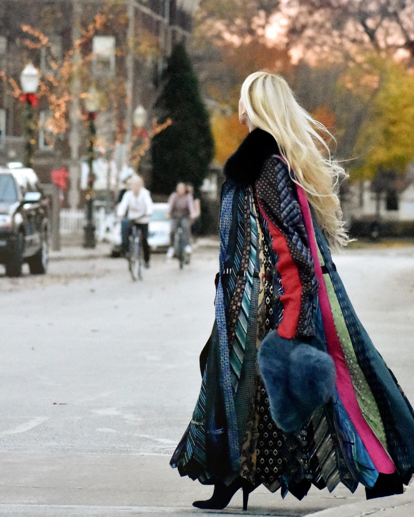Blonde woman walking across a street while wearing a long multi-color coat