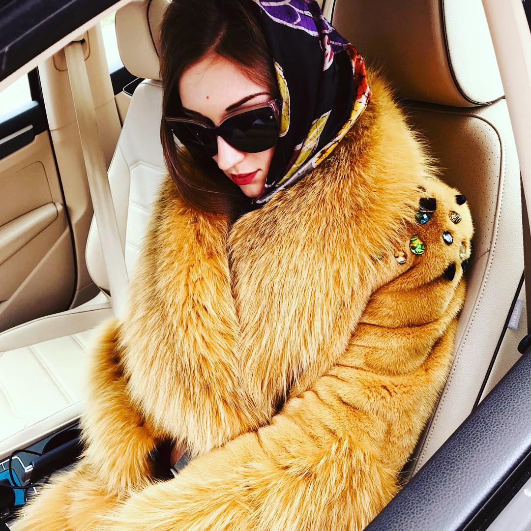 Woman wearing a natural red fox fur coat and a head covering while in a car