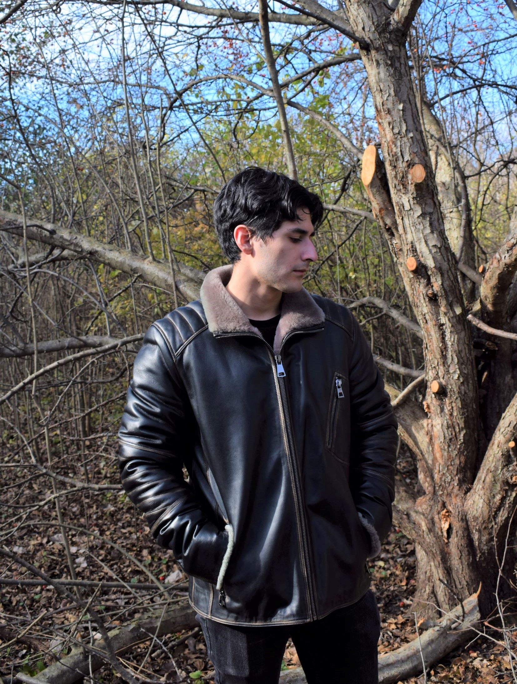 Man wearing a leather jacket lined with fur standing in a wooded area