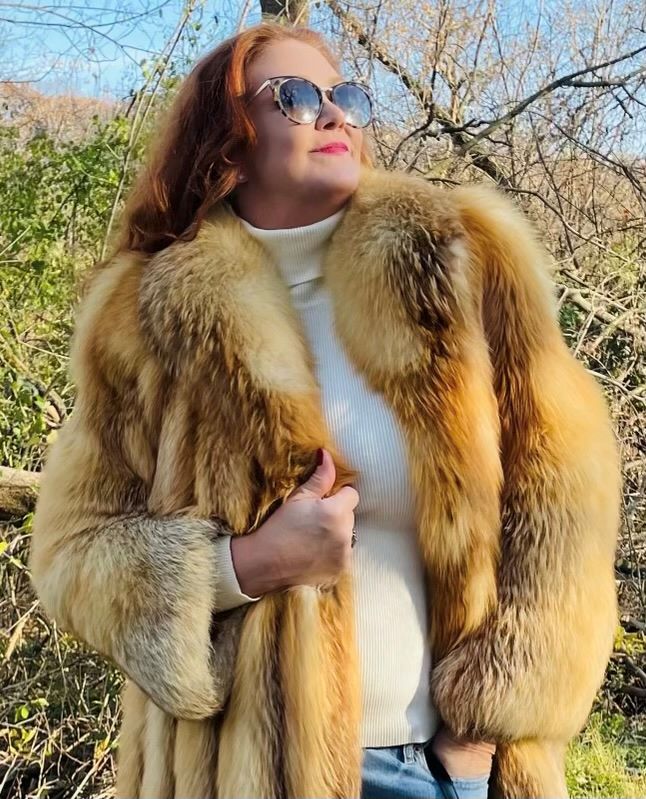 Woman standing in a wooded area while wearing a natural red fox fur jacket