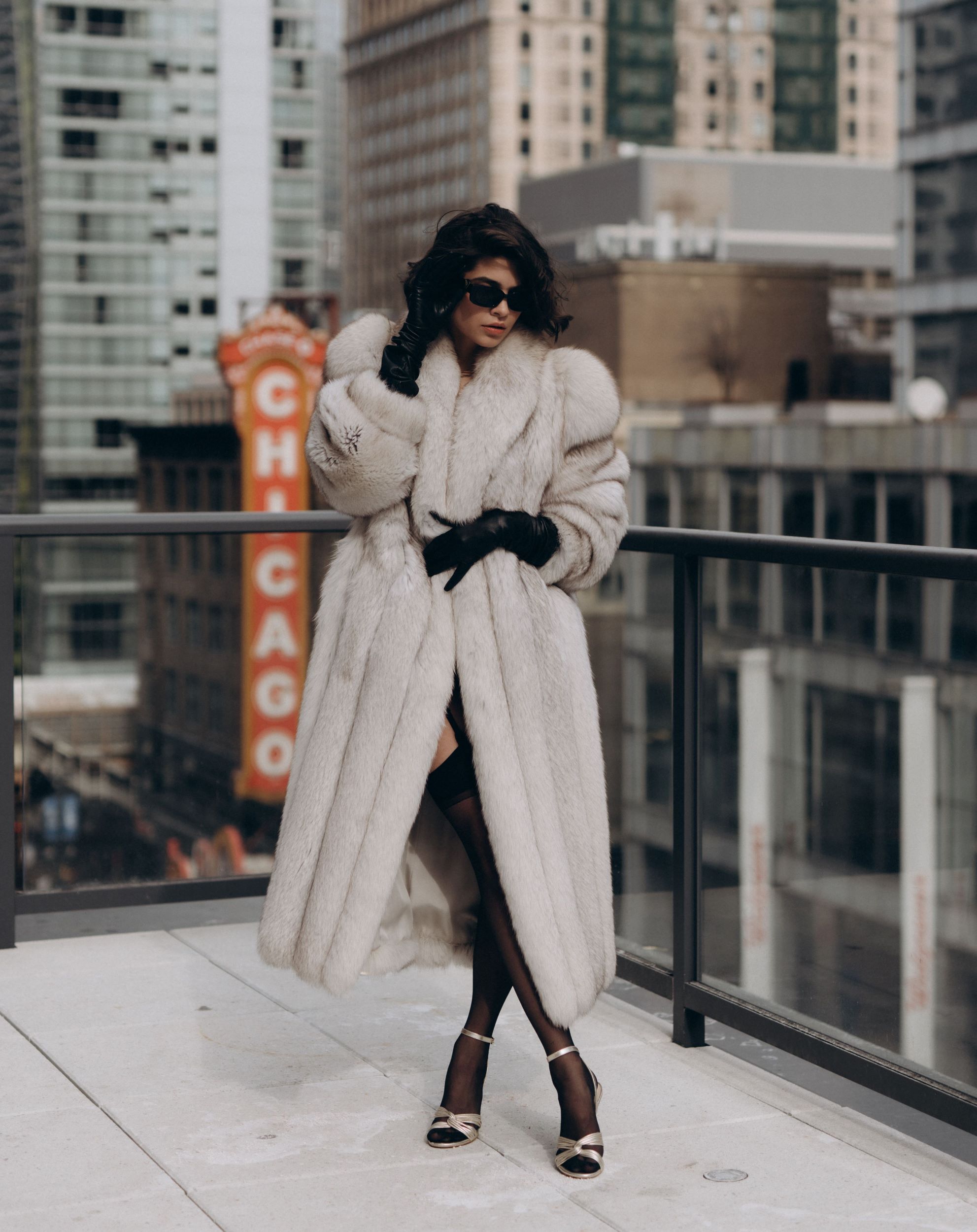 Fashionable woman standing atop a building with a luscious white fur coat