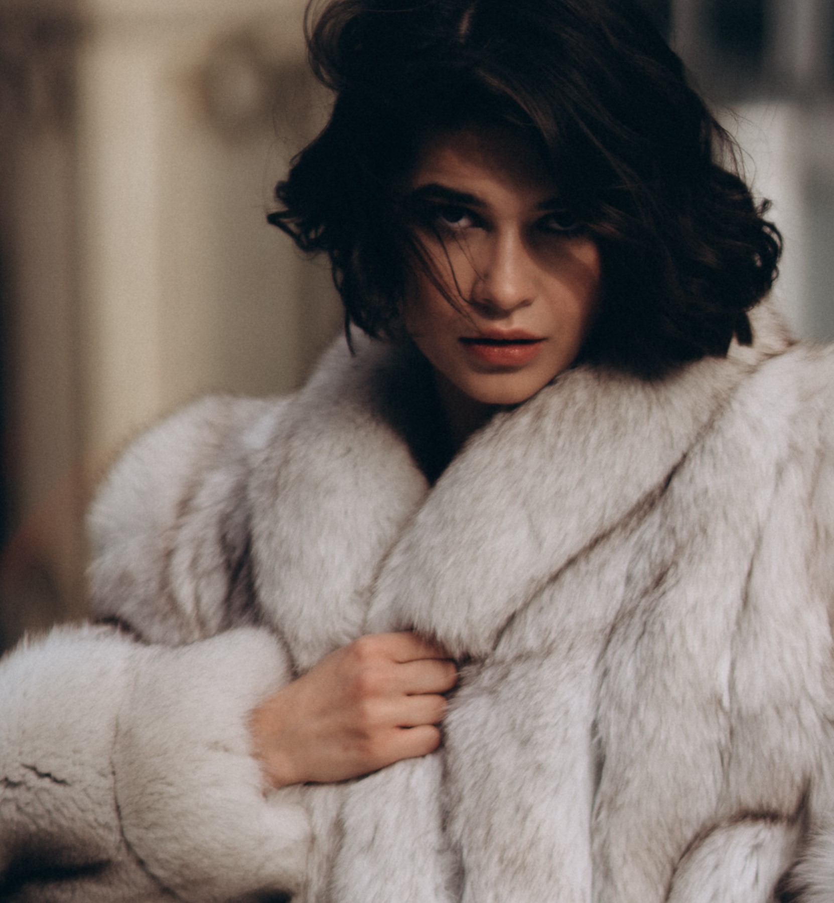 Woman with black hair grasping her white fur coat with one hand