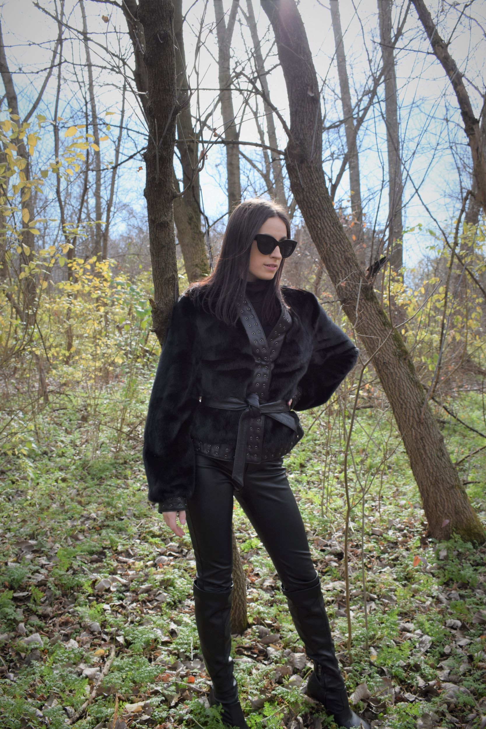 Woman posing with hand on hip in forest while wearing a fur coat and black leather pants
