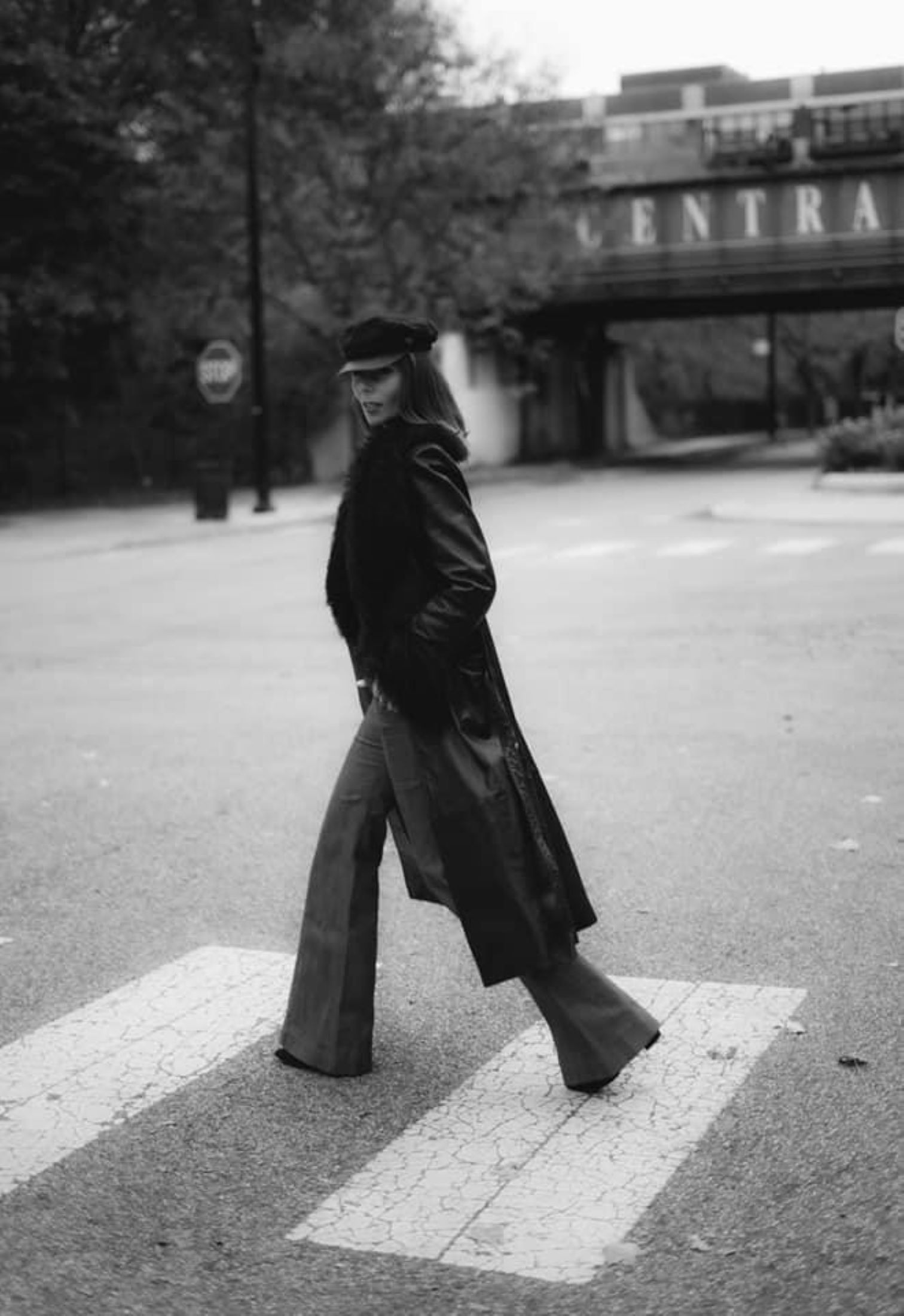 Woman walking across a cross walk while wearing a black leather coat and bell bottom pants