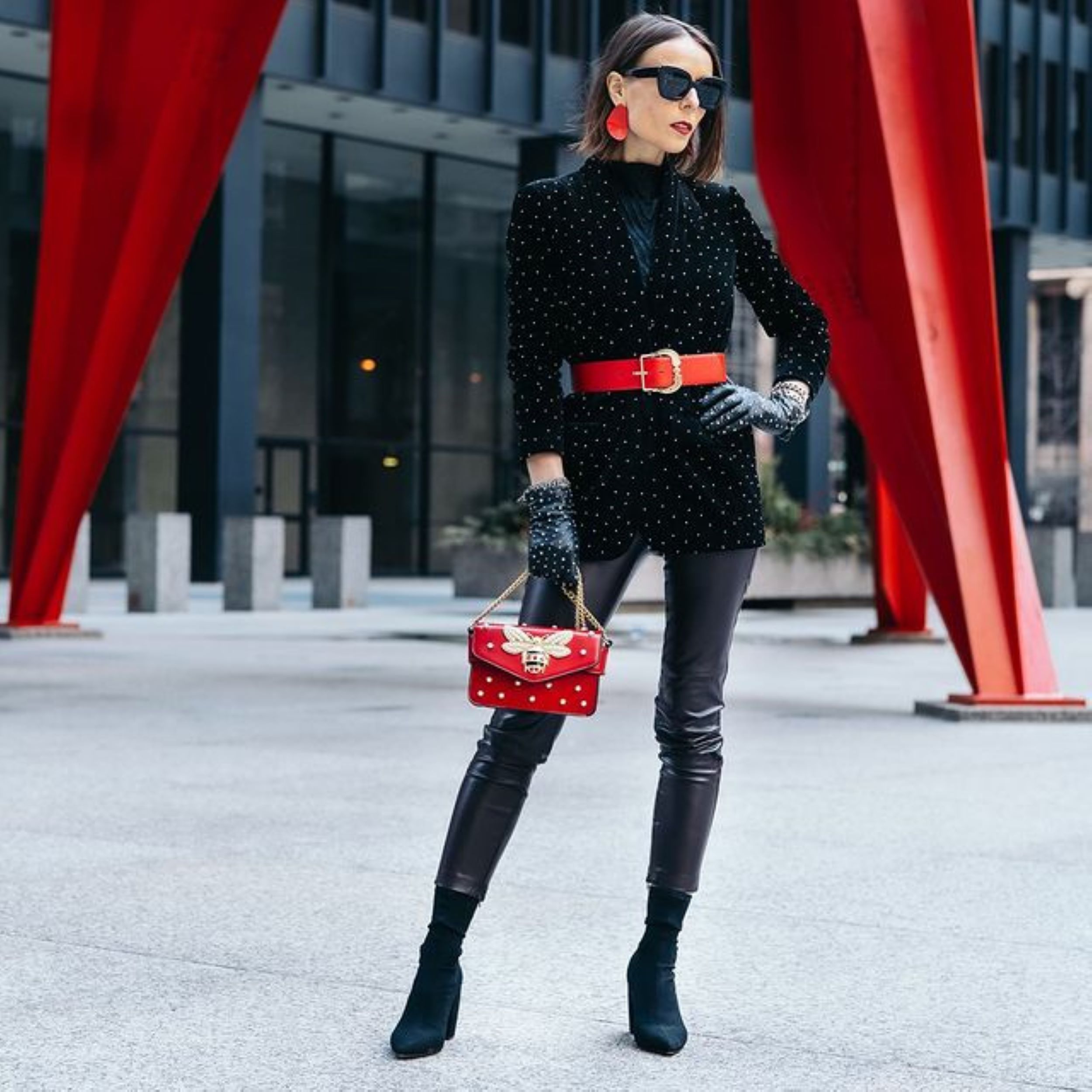 Chic woman in a black sparkly coat with a red waist belt and a small red purse